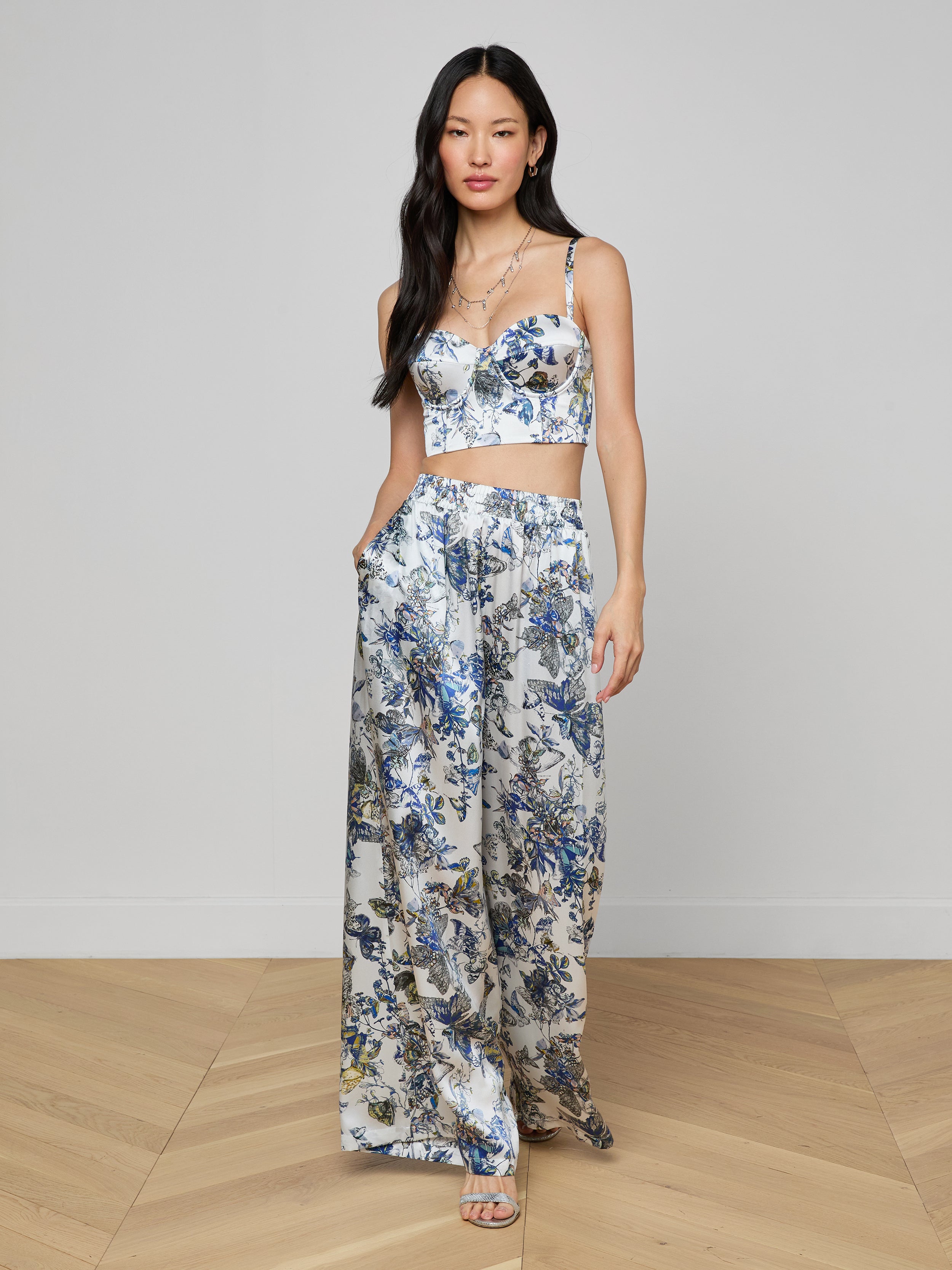 A woman stands with her hands in her pockets against a plain light background, wearing the Sonya Silk Bustier paired with matching wide-leg pants featuring a butterfly print.