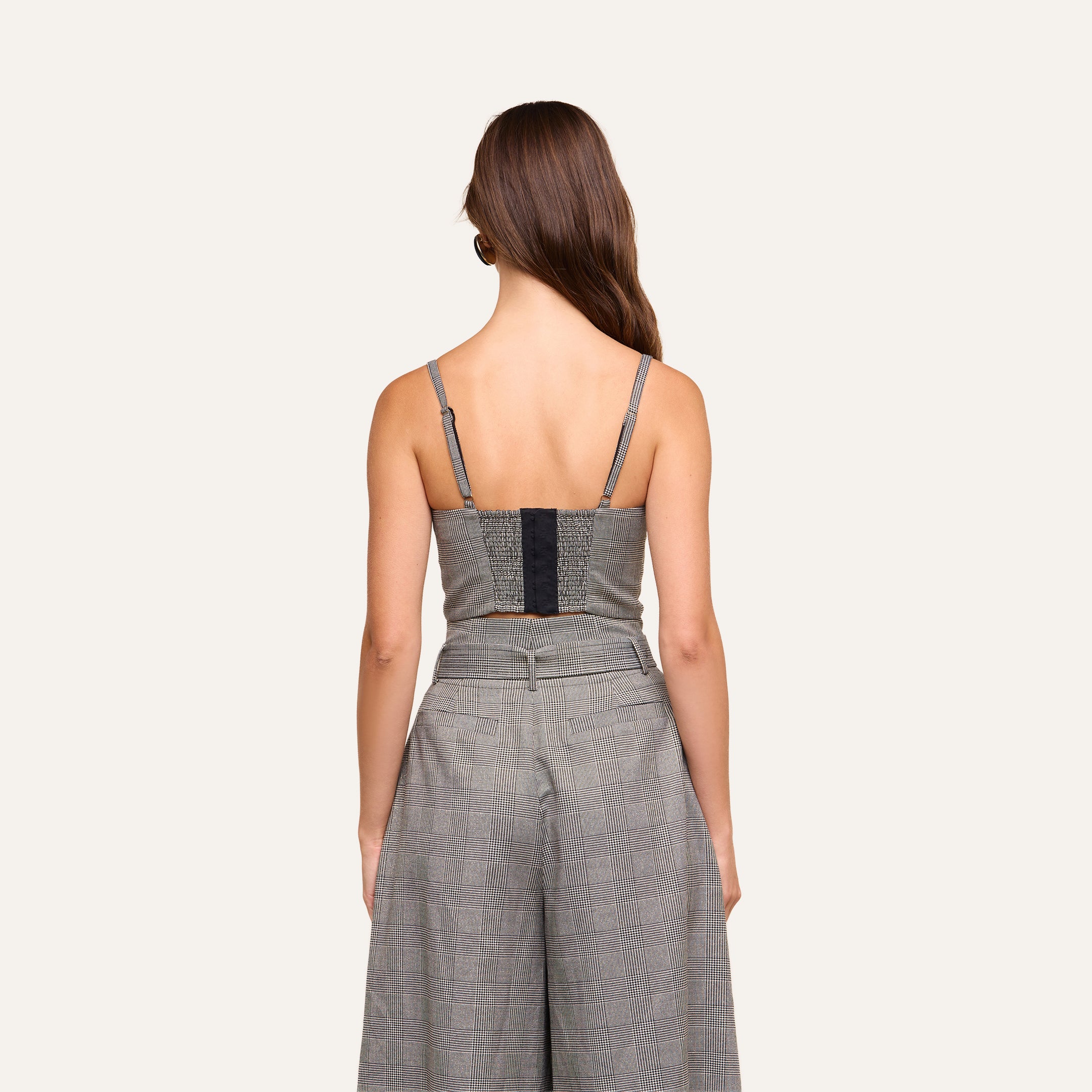 A woman with long brown hair stands facing away, wearing the sleeveless Sonya Bustier with built-in support and matching high-waisted pants against a plain light background.