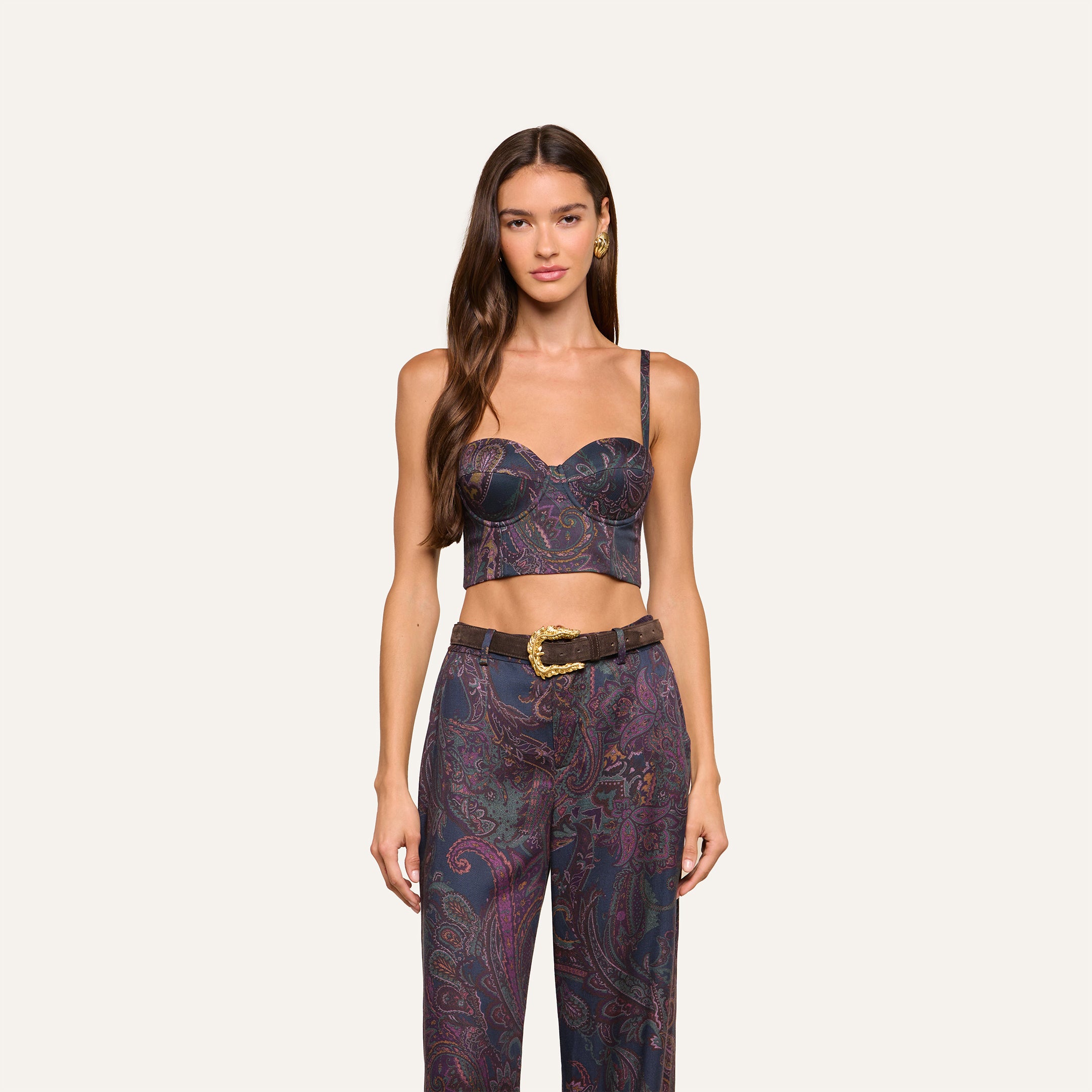 A woman with long brown hair wears the Sonya Bustier in navy paisley, paired with matching high-waisted pants and a wide brown belt, standing against a plain off-white background.