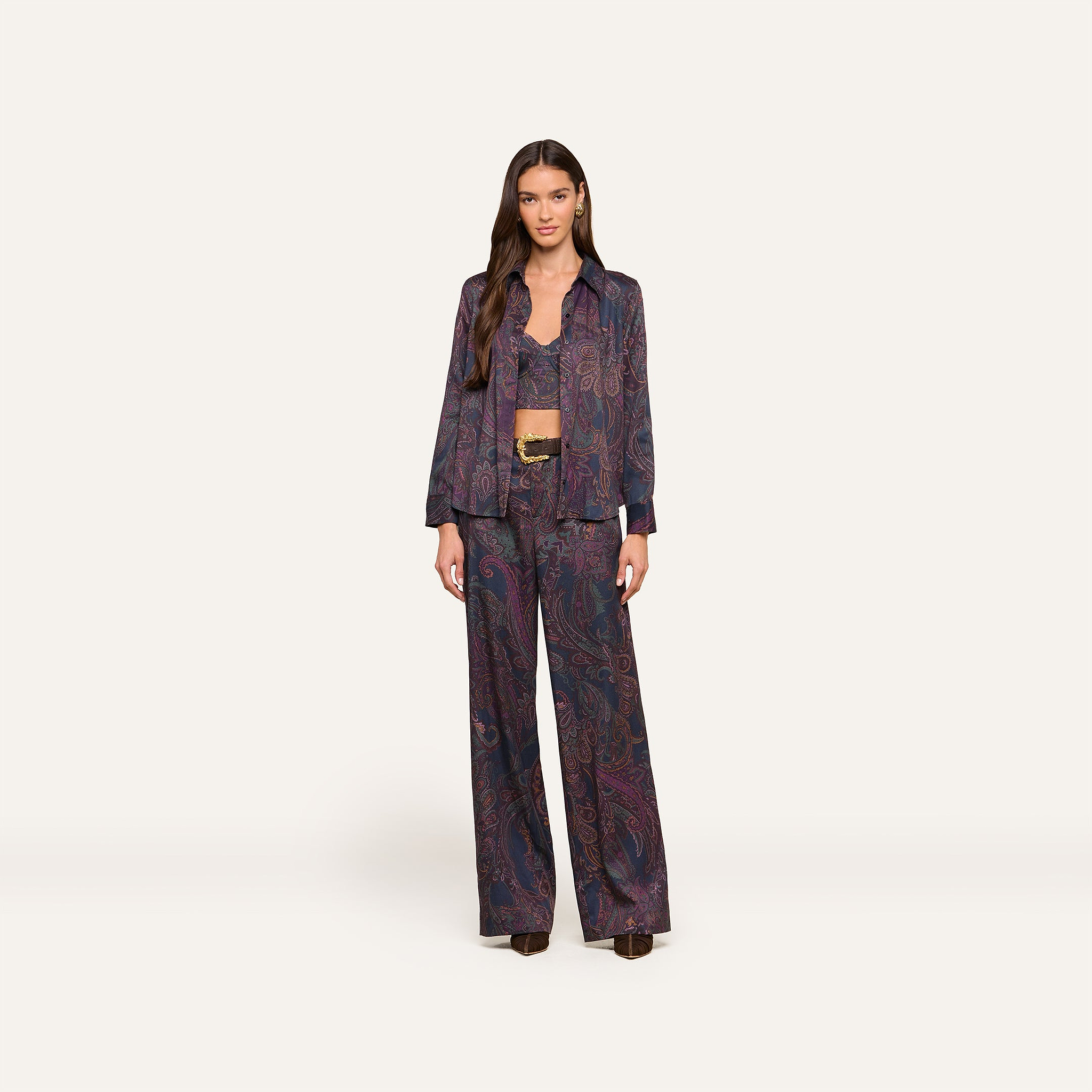 A woman stands facing forward, wearing the Sonya Bustier in a matching navy paisley-patterned suit with wide-leg pants, a buttoned shirt, and a belt. She has long hair and a neutral expression. The background is plain and light.