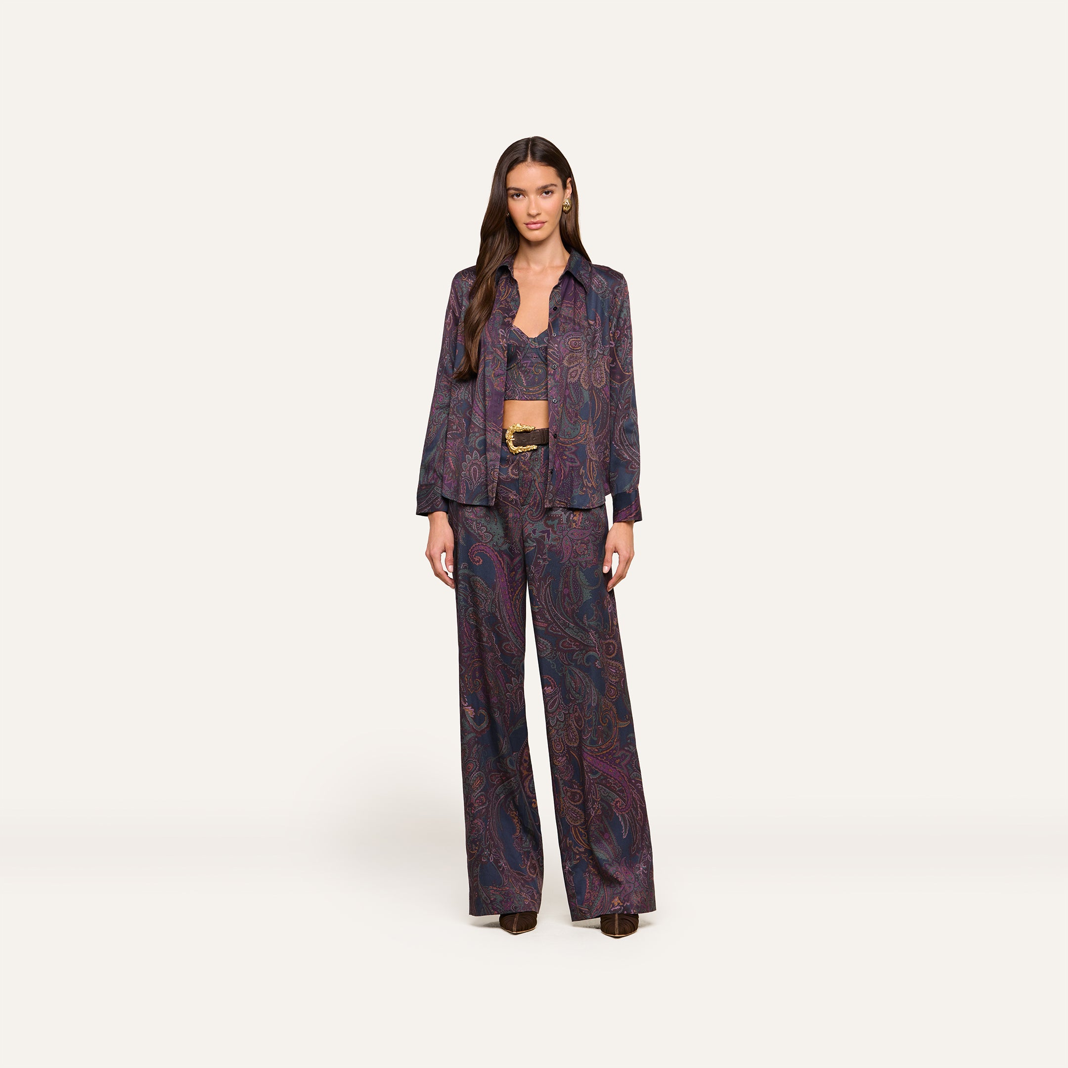 A woman stands facing forward, wearing the Sonya Bustier in a matching navy paisley-patterned suit with wide-leg pants, a buttoned shirt, and a belt. She has long hair and a neutral expression. The background is plain and light.