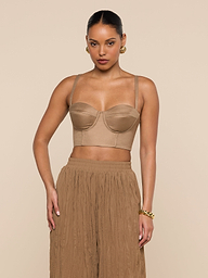 A woman wearing the Sonya Linen-Blend Bustier with high-waisted, loose tan pants stands against a plain, light background. She accessorizes with gold hoop earrings and a gold bracelet, and her hair is tied back.