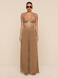 A woman wearing sunglasses, the Sonya Linen-Blend Bustier with adjustable straps, and wide-legged brown pants stands against a plain white background.