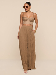 Wearing the Sonya Linen-Blend Bustier, a woman in sunglasses and high-waisted, wide-leg brown pants stands confidently against a white background with one hand in her pocket.