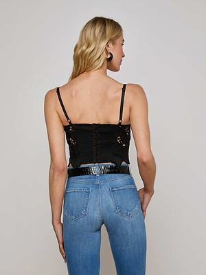 A woman with long blonde hair wears the L'AGENCE Sale Sonya Eyelet Bustier with underwire cups and high-waisted blue jeans, standing facing away from the camera against a plain light background.