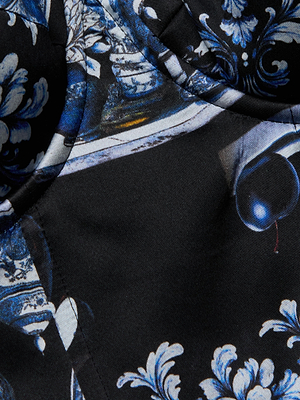 A close-up of the L'AGENCE Sonya Silk Bustier shows its blue and white porcelain floral print and a realistic dark purple plum on black silk charmeuse, with visible stitching details.