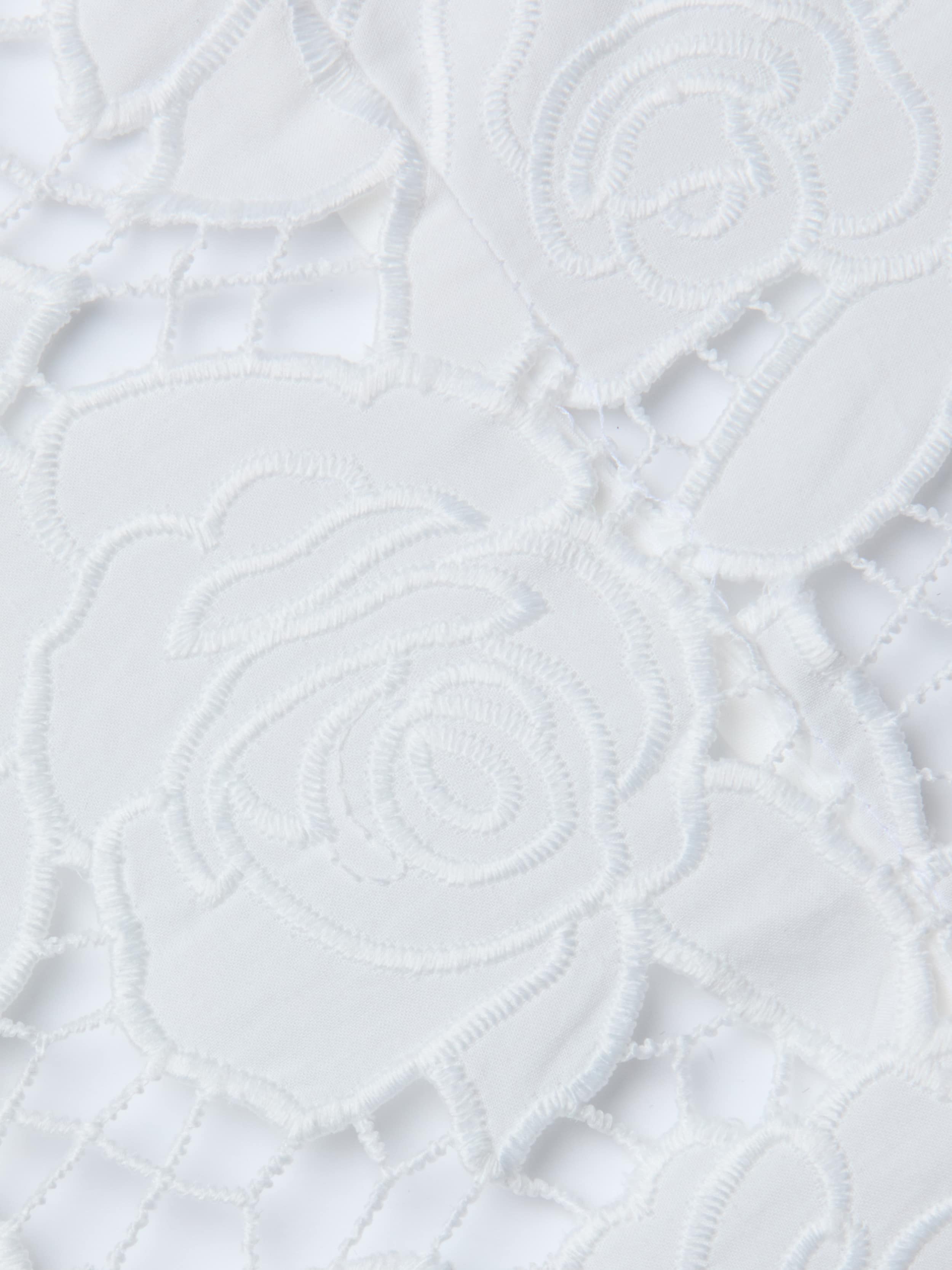 Close-up of the Sonya Bustier, featuring white lace fabric with an intricate floral rose pattern, showcasing delicate embroidery and openwork details reminiscent of a cotton bustier top with underwire cups, all set against a white background.