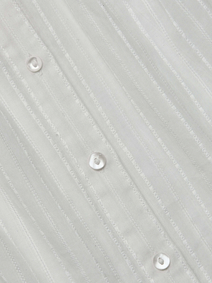 Close-up of the L'AGENCE Kiera Blouse features semi-sheer jacquard white fabric with subtle vertical stripes, small white buttons sewn diagonally, and alternating matte and shiny textured lines.