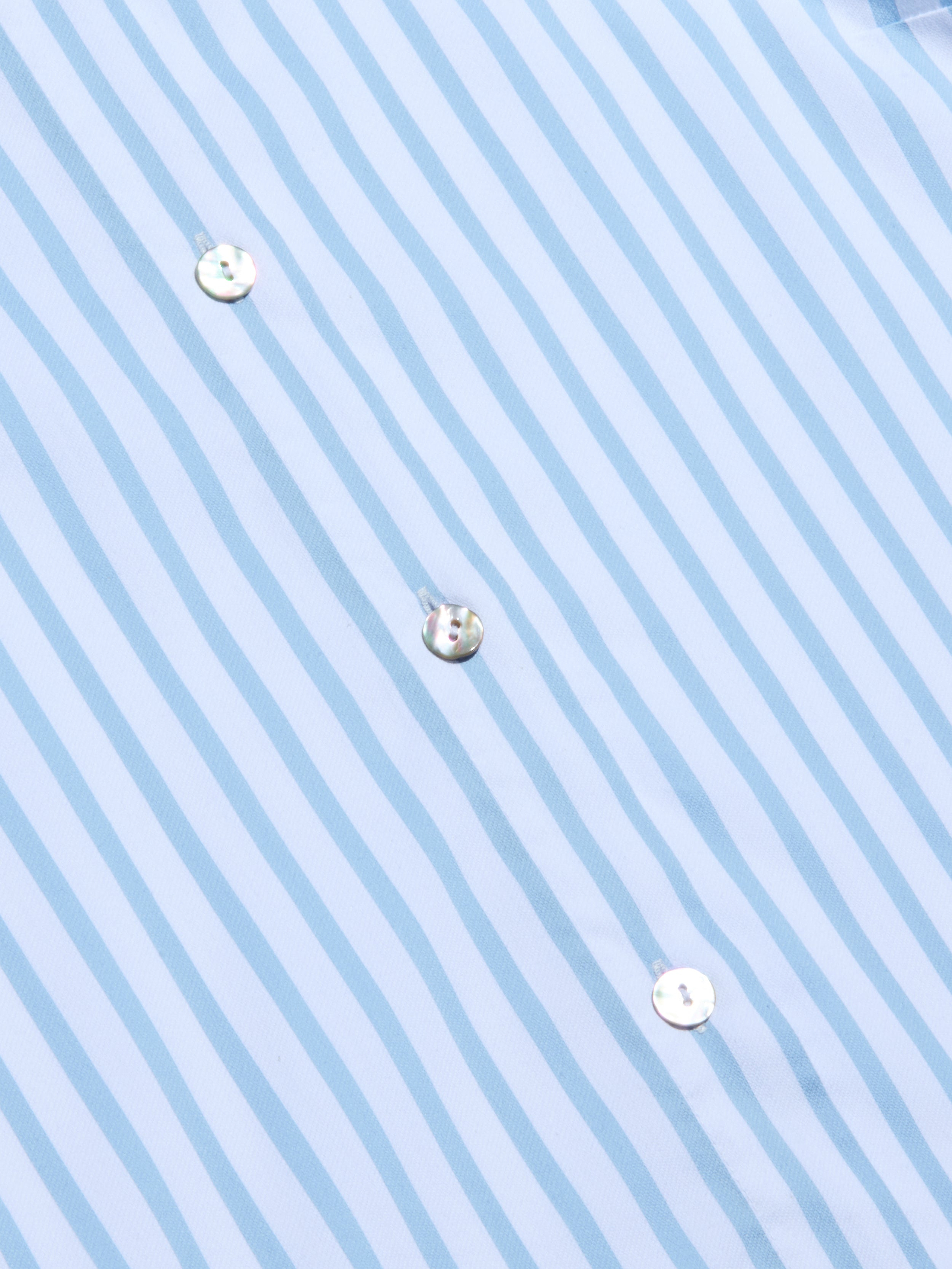 Gros plan sur la chemise Fawn Beach Print en coton biologique, avec des rayures verticales bleu clair et blanches et trois boutons blancs visibles. Les rayures sont régulièrement espacées pour un aspect net et précis.