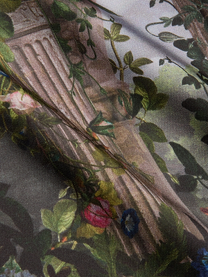 A close-up of the Fawn Floral Print Shirt shows organic cotton fabric with detailed foliage, flowers, and a stone column design. The visible texture and folds create depth and shadow in the floral print.