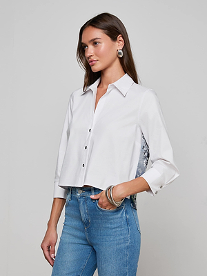 A woman with straight brown hair models the Fawn Panther Print Shirt, styled cropped like a button-down, paired with blue jeans. She accessorizes with hoop earrings and chunky bangles, standing against a light gray background.