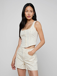 A woman poses against a plain light background, wearing the sleeveless cream Saga Top with nautical stripes and matching high-waisted shorts, one hand casually in her pocket.