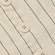 Close-up of the Saga Top, showcasing its off-white cotton twill fabric with thin black nautical stripes and four round buttons, each featuring four holes and text around the edges.