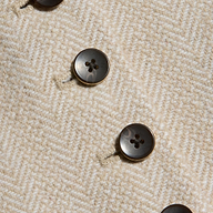 Close-up of four black buttons on textured, beige herringbone tweed fabric from the Jianna Vest, arranged in diagonal rows with visible stitching around the buttonholes.