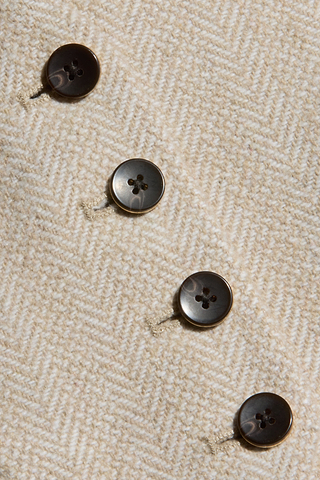 Four dark brown, four-hole buttons are sewn diagonally onto beige herringbone tweed on the Jianna Vest, attached with light-colored thread for a refined finish inspired by New York Fashion Week.