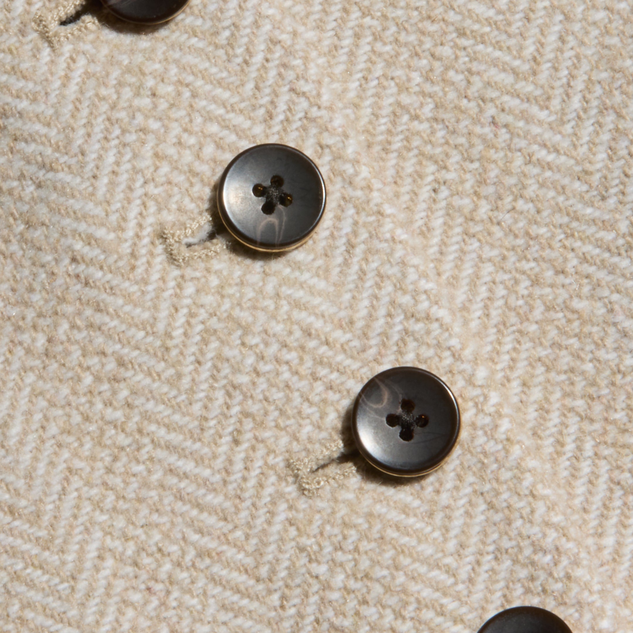 Close-up of four black buttons on textured, beige herringbone tweed fabric from the Jianna Vest, arranged in diagonal rows with visible stitching around the buttonholes.