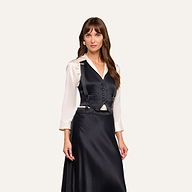 A woman stands wearing a cream blouse, the Jianna Vest—a tailored black pinstripe vest with buttons—and a matching black skirt. She has long brown hair and a neutral expression, posing against a plain light background.