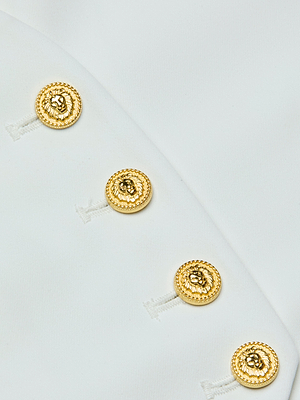 Close-up of the Jianna Vest’s white fabric adorned with four gold lion’s head buttons arranged diagonally—a signature detail that enhances the vest’s minimalist silhouette.
