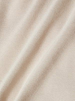 A close-up of soft, light beige satin with gentle diagonal folds and a subtle texture, capturing the romantic elegance of the L'AGENCE Bernice Satin Wrap Blouse.