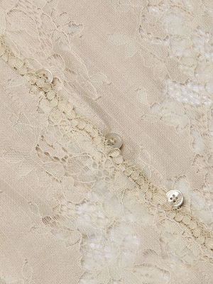 Close-up of the Anita Lace Blouse in beige, highlighting its delicate floral lace pattern and a row of small, round, semi-transparent buttons along the edge.