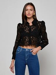 A woman wearing the Anita Lace Blouse—a long-sleeve, black floral lace top with a collar and puffed shoulders—paired with high-waisted blue jeans, stands against a plain light background.