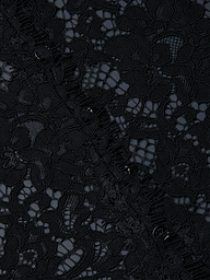 Close-up of the Anita Lace Blouse’s intricate black lace fabric, featuring a delicate floral pattern, detailed stitching, and mesh accents, with a scalloped hem and a subtly sheer background.