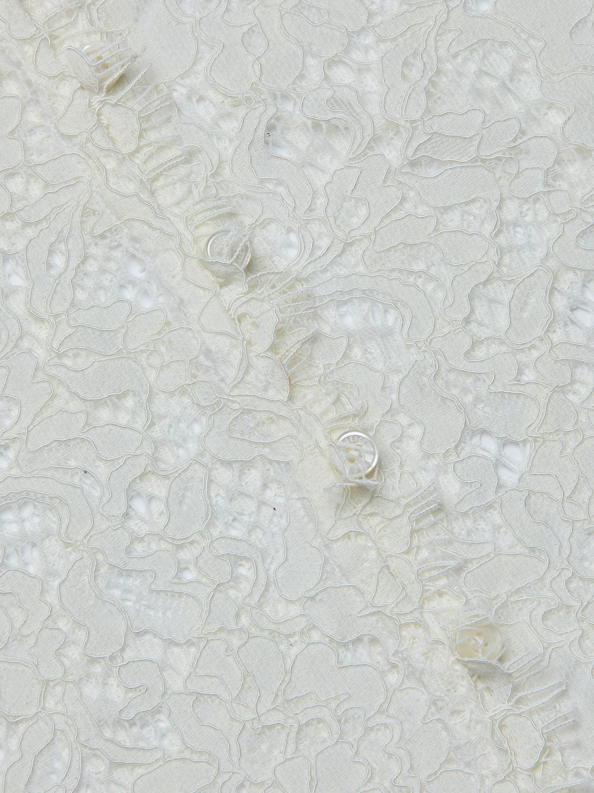 Close-up of the Anita Lace Blouse, featuring delicate white lace fabric with intricate floral patterns and textured, raised embroidery on a sheer background, evoking a romantic, feminine style.