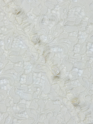 Close-up of the Anita Lace Blouse: textured off-white floral lace with a raised pattern. Diagonal seam features several matching fabric-covered buttons for a delicate, intricate, and elegant look.