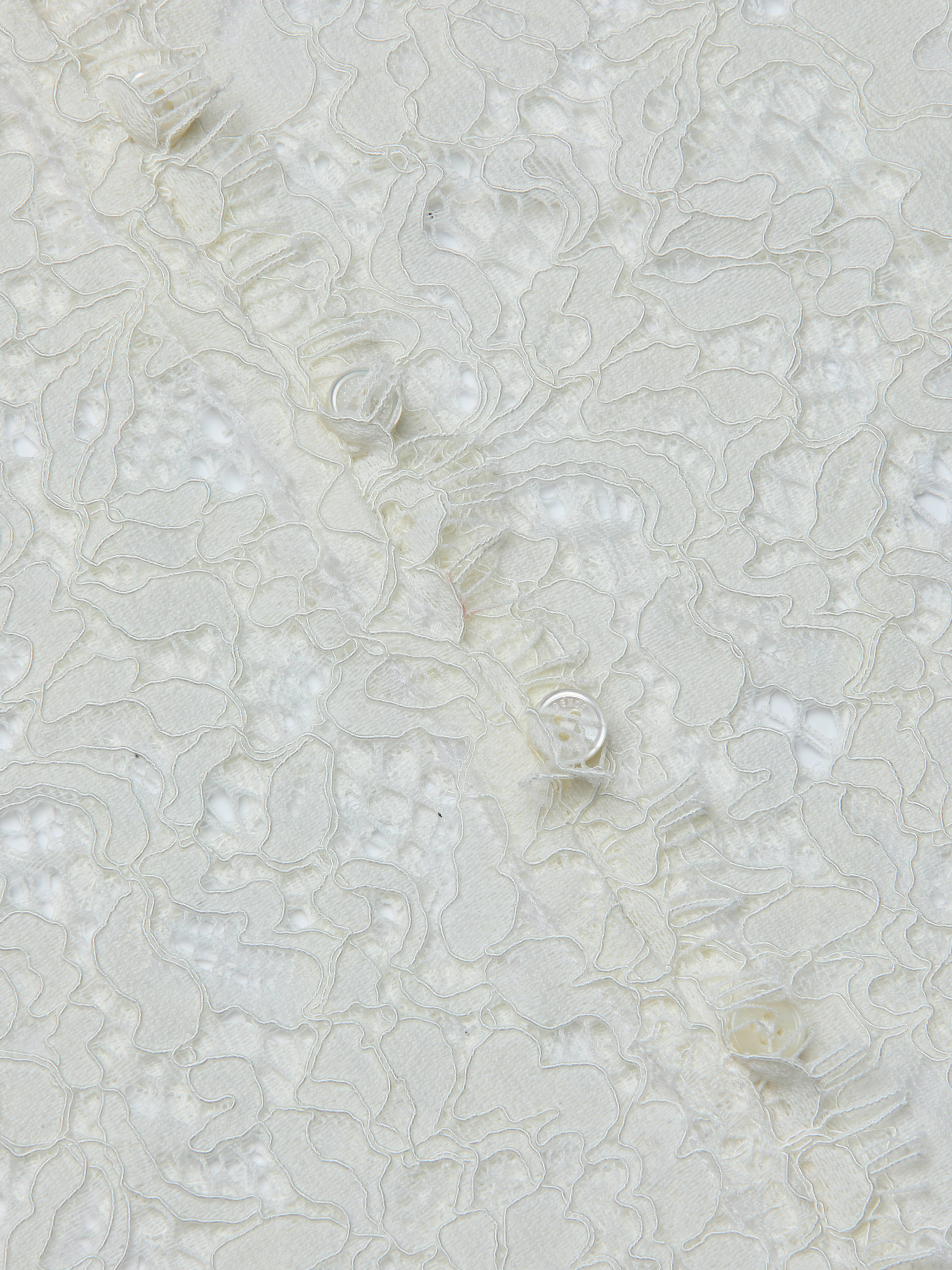 Close-up of the Anita Lace Blouse, featuring delicate white lace fabric with intricate floral patterns and textured, raised embroidery on a sheer background, evoking a romantic, feminine style.
