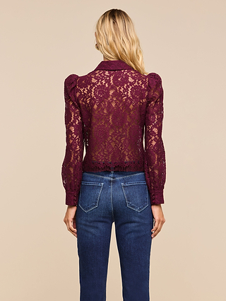 A woman is seen from behind wearing the Anita Lace Blouse, a sheer burgundy cropped top with floral lace and puffed sleeves, paired with blue jeans, standing against a plain beige background.