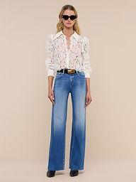 A woman wearing sunglasses, the Anita Lace Blouse, blue high-waisted wide-leg jeans, and black shoes stands against a plain white background.