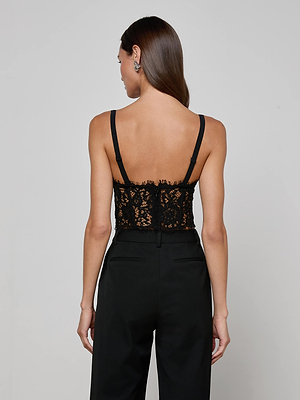 A woman with long brown hair, seen from the back, wears the L'AGENCE Raquel Lace Bustier and high-waisted black pants against a plain, light background.