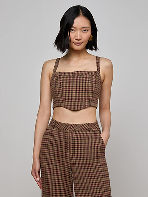 A woman with short black hair models the L'AGENCE Tiffany Corset Top, featuring a cotton houndstooth print, paired with matching high-waisted pants. She stands against a plain light gray background with one hand in her pocket.