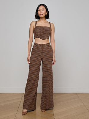 A woman with shoulder-length dark hair poses indoors against a light gray wall and wooden floor, wearing the L'AGENCE Tiffany Corset Top in brown houndstooth print with matching high-waisted wide-leg pants and brown heels.