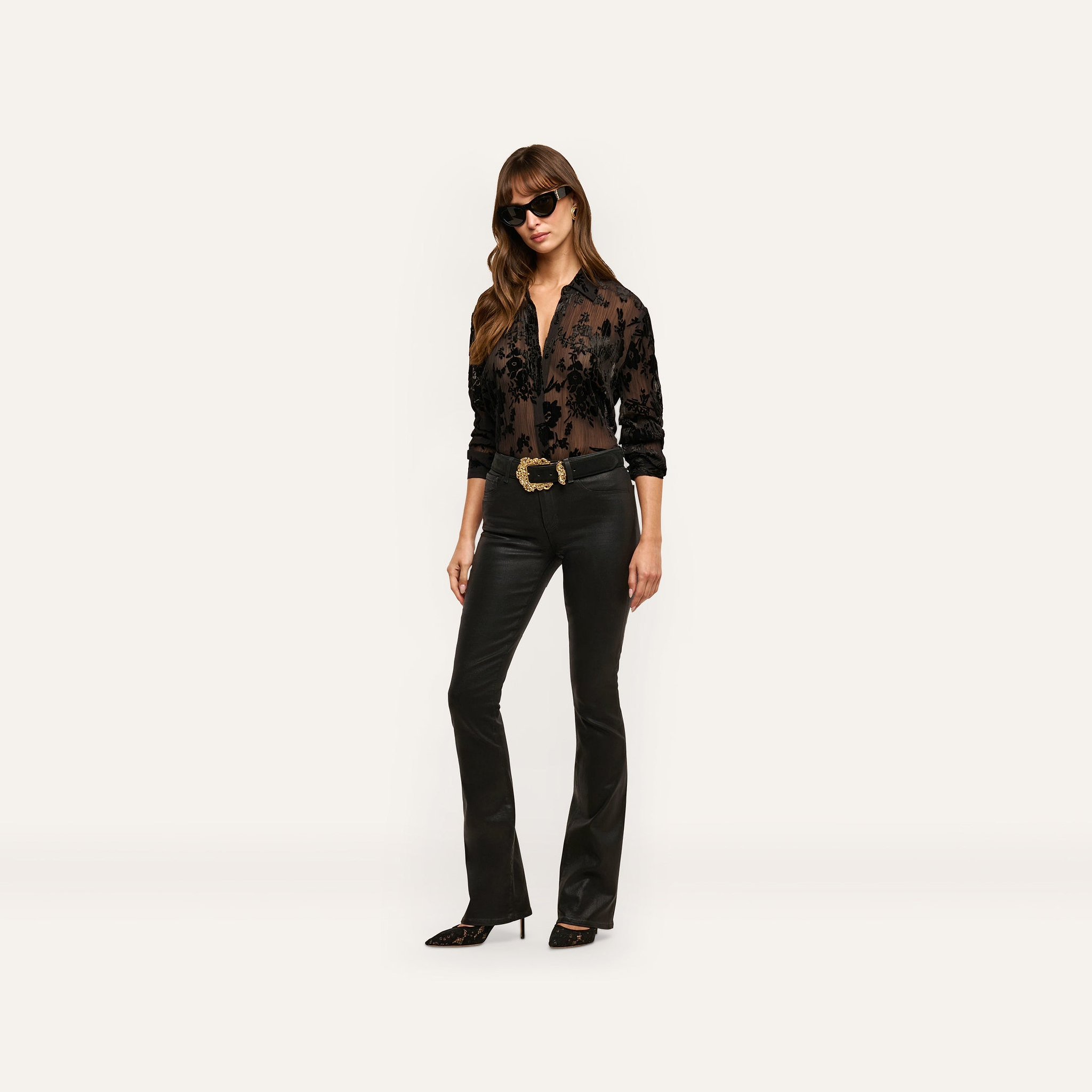 A person wears a black, sheer devoré velvet Laurent Velvet Blouse, black slim-fit trousers with a wide gold belt buckle, dark sunglasses, and pointed-toe heels.