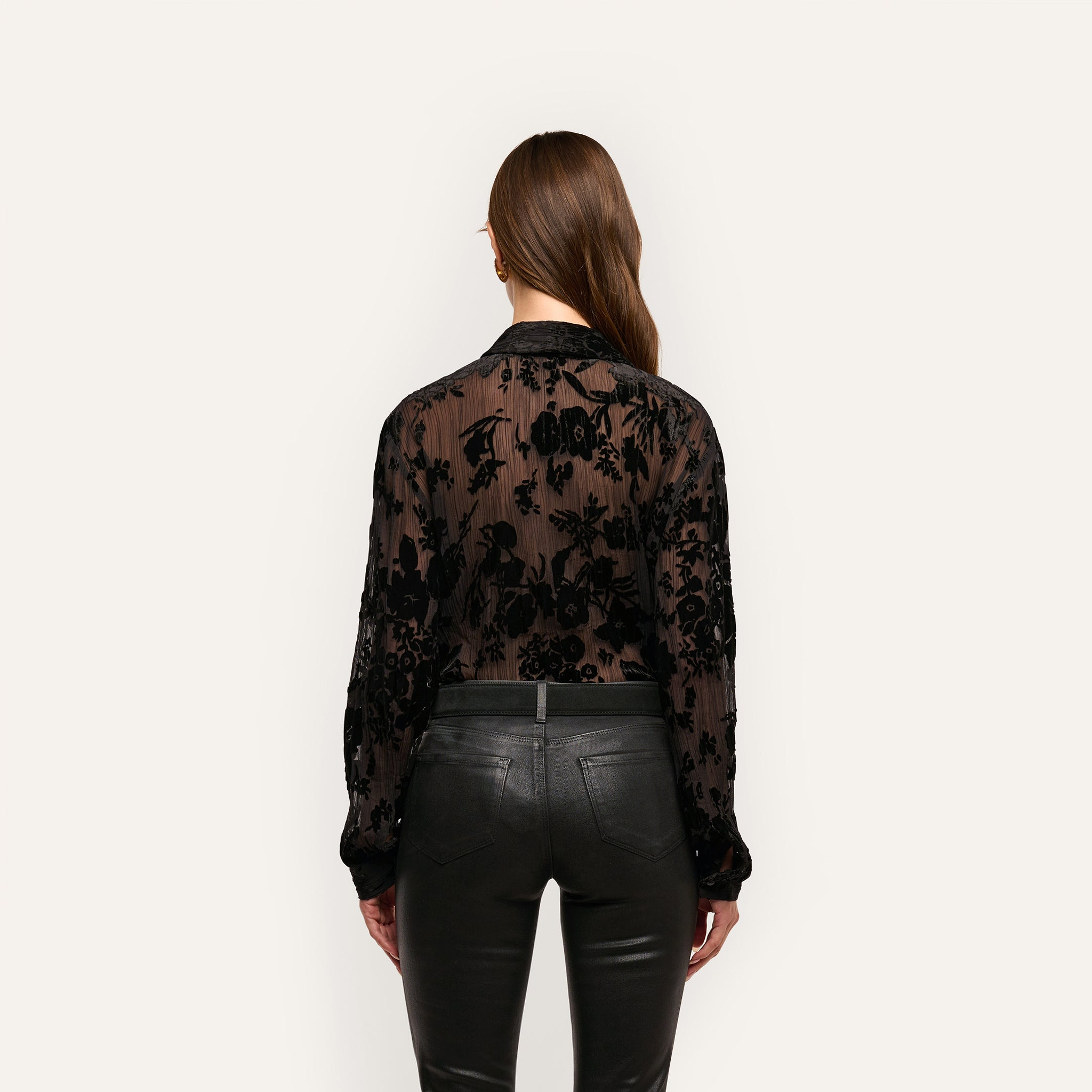 Back view of a person wearing a sheer black devoré velvet Laurent Velvet Blouse with a floral pattern, paired with black pants.