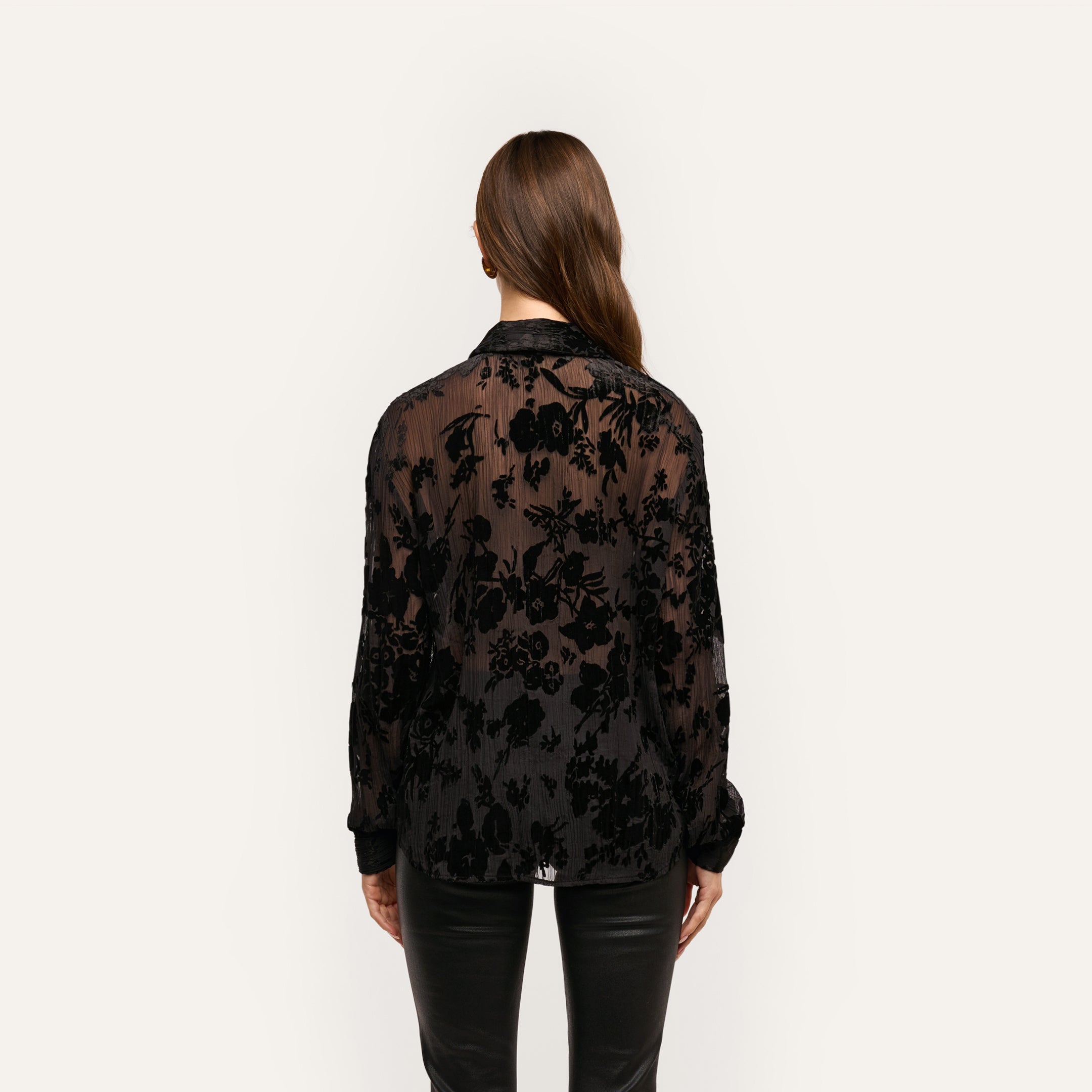 Back view of a person wearing a sheer black Laurent Velvet Blouse with a crinkle velvet floral pattern in a relaxed, button-down fit.