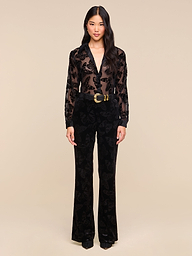 A woman stands facing forward against a plain white background, wearing the Laurent Velvet Blouse—a sheer burnout velvet top with a floral pattern—paired with black pants, a wide black belt featuring a gold buckle, and black shoes.