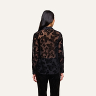 A woman with long dark hair faces away, wearing the Laurent Velvet Blouse—a relaxed fit button-down with a butterfly devoré pattern—and black pants, standing against a plain light background.