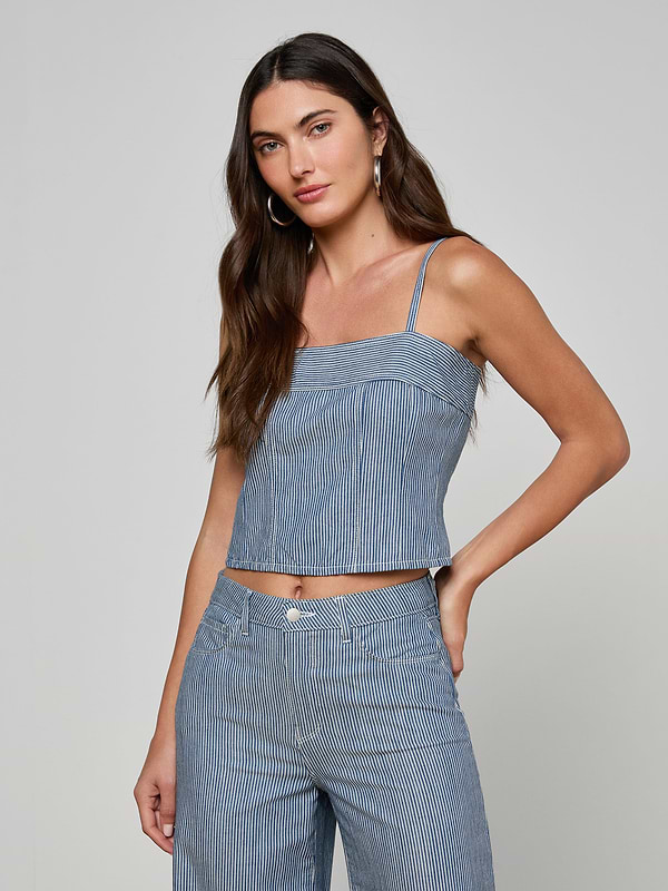 A woman with long brown hair is wearing the Arlin Tank—a blue striped sleeveless top—paired with matching pants, standing with one hand on her hip against a plain light background.