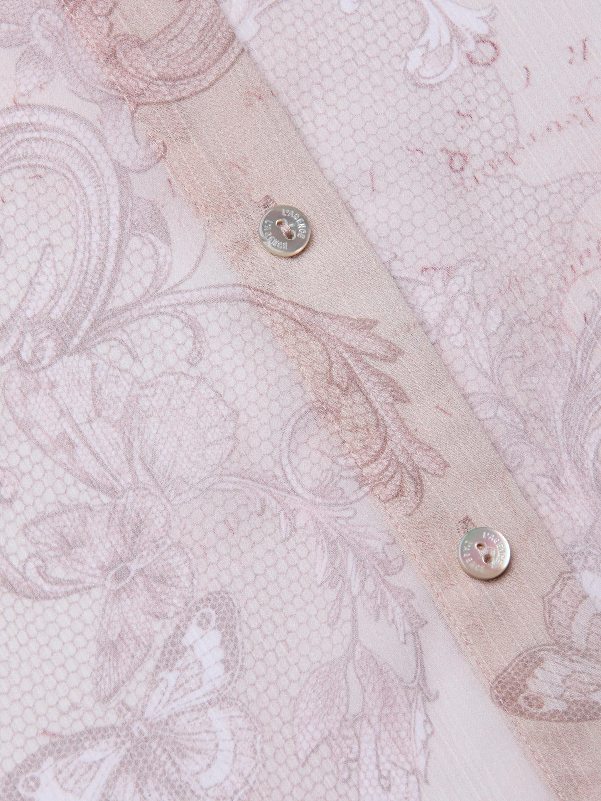 Close-up of the Laurent Blouse in sheer light pink poly chiffon, featuring intricate floral and butterfly patterns, visible stitching, and two metallic buttons along the seam.