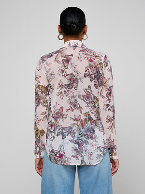 A person with dark hair in a bun wears the Laurent Blouse, featuring a relaxed fit and butterfly jungle print, paired with light blue jeans, standing with their back to the camera against a plain light background.