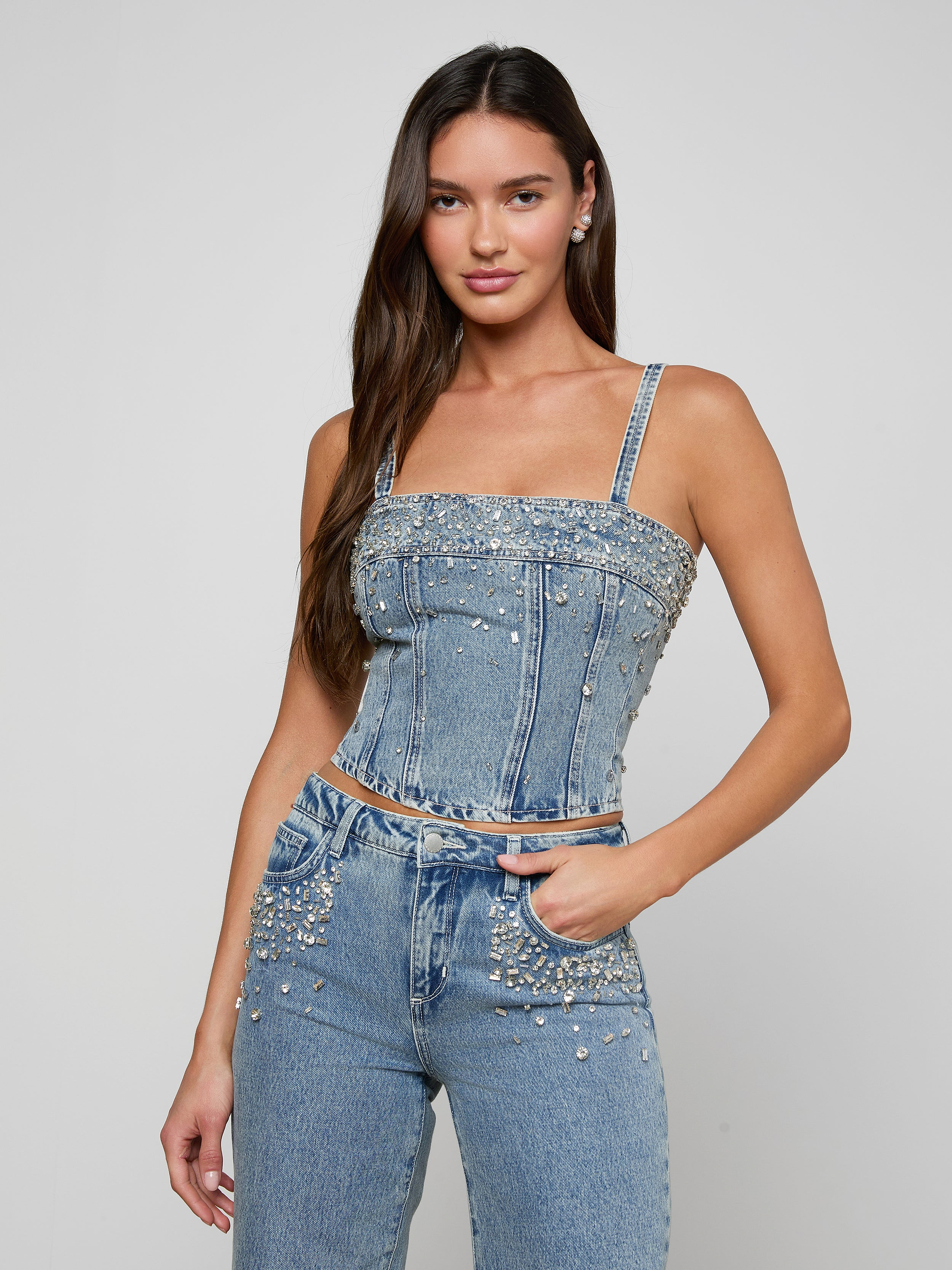 Woman wearing a sparkly denim top and jeans on a plain background