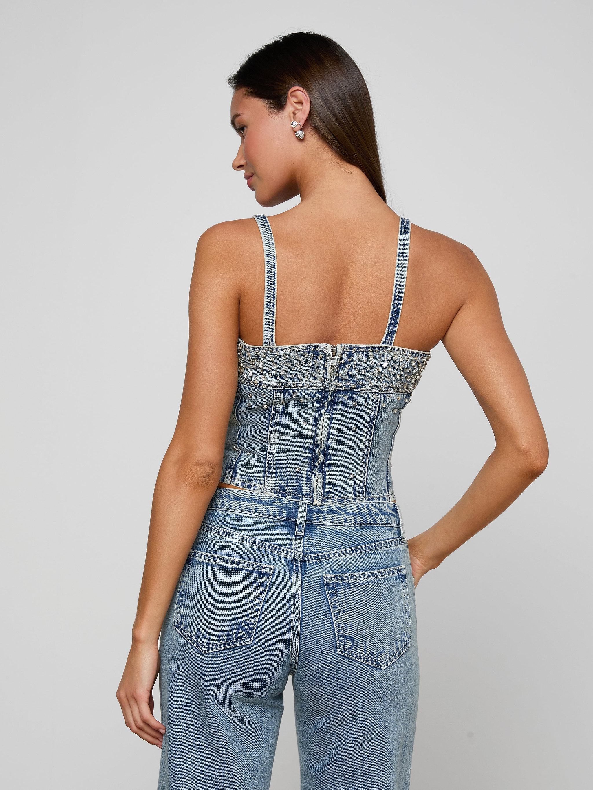 Woman wearing a denim embellsihed top on a plain background