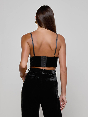 A woman with long brown hair models the L'AGENCE Aislin Velvet Bralette, a black crop top with adjustable straps, viewed from the back against a plain light gray background.