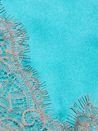Close-up of the Kimber Silk Lace Camisole, showcasing delicate beige lace with intricate floral patterns against a smooth, bright turquoise background. The camisole’s frayed edges create a soft contrast with the vibrant, solid-colored fabric beneath.