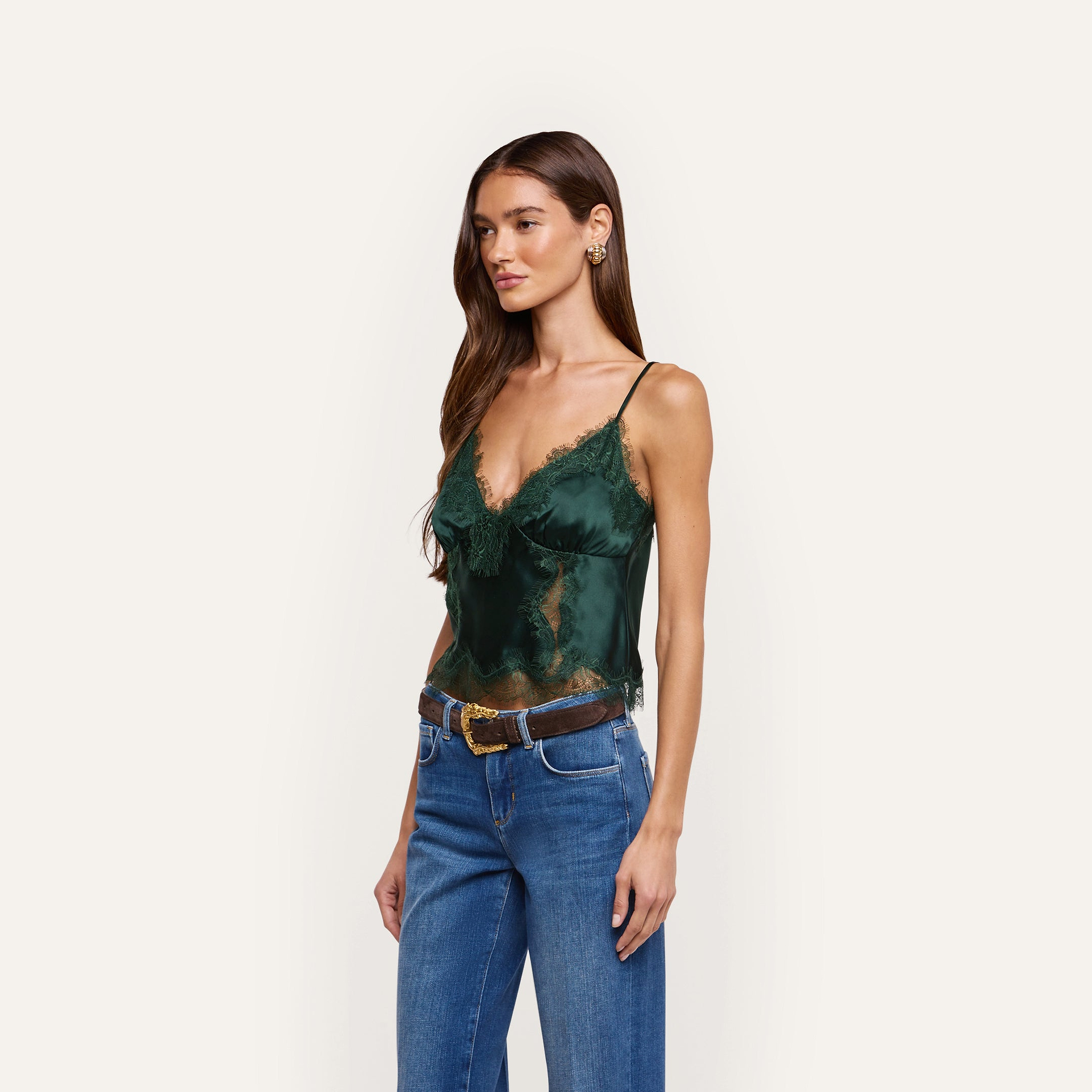 A person wearing a Kimber Silk Lace Camisole with a deep V-neckline and lace trim, paired with blue jeans and a brown belt.