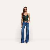 A person wearing a dark green lace-trimmed Kimber Silk Lace Camisole with a deep V-neckline, wide-leg blue jeans with a brown belt, and sunglasses.