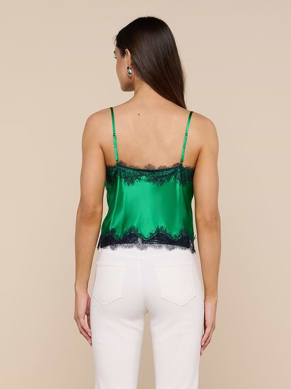 A woman is seen from behind wearing the Kimber Silk Lace Camisole in green with black trim, paired with white pants against a plain light backdrop.