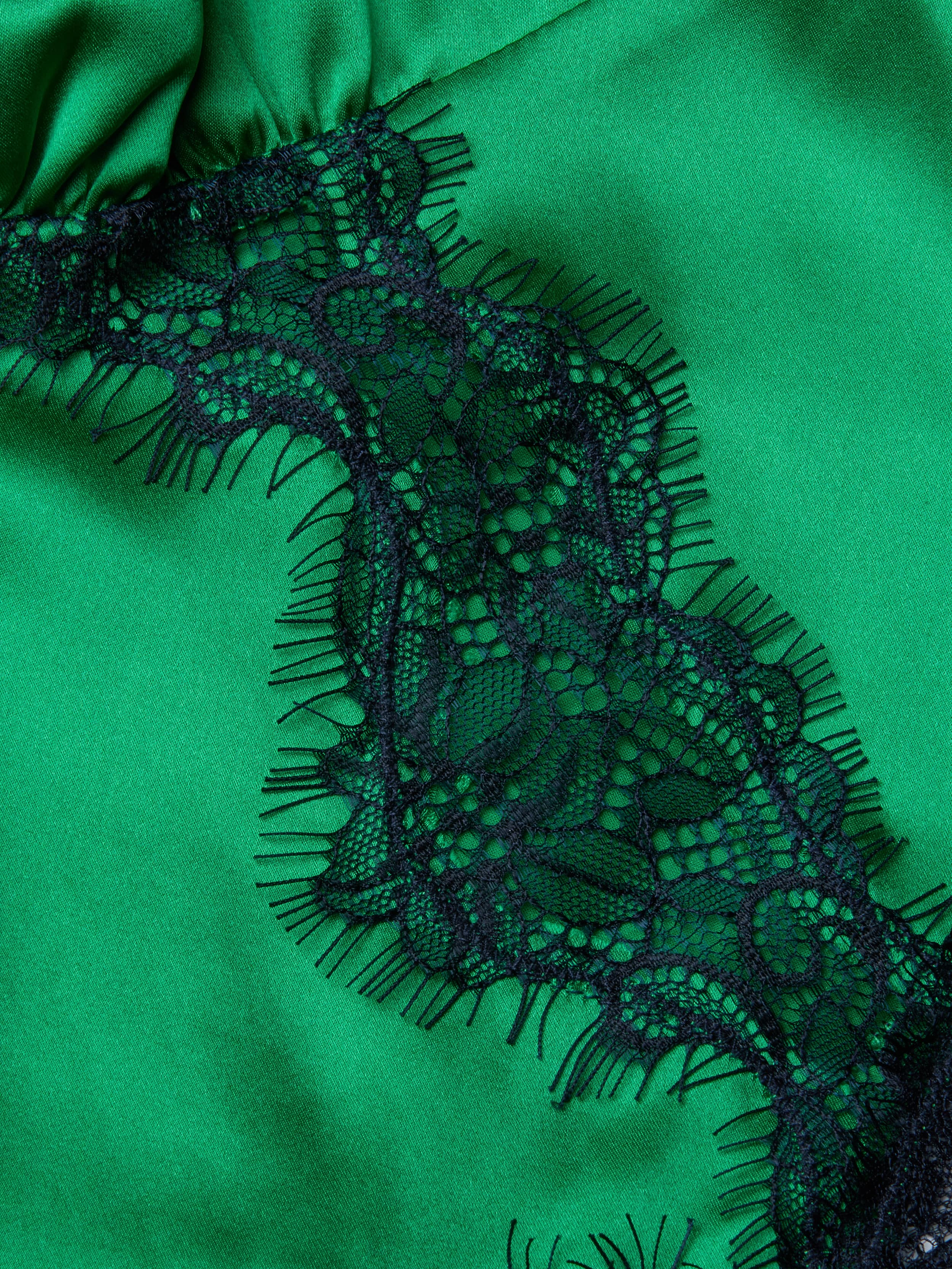 Close-up of the Kimber Silk Lace Camisole, showcasing green satin fabric with a black lace trim adorned with a floral pattern and delicate fringe.